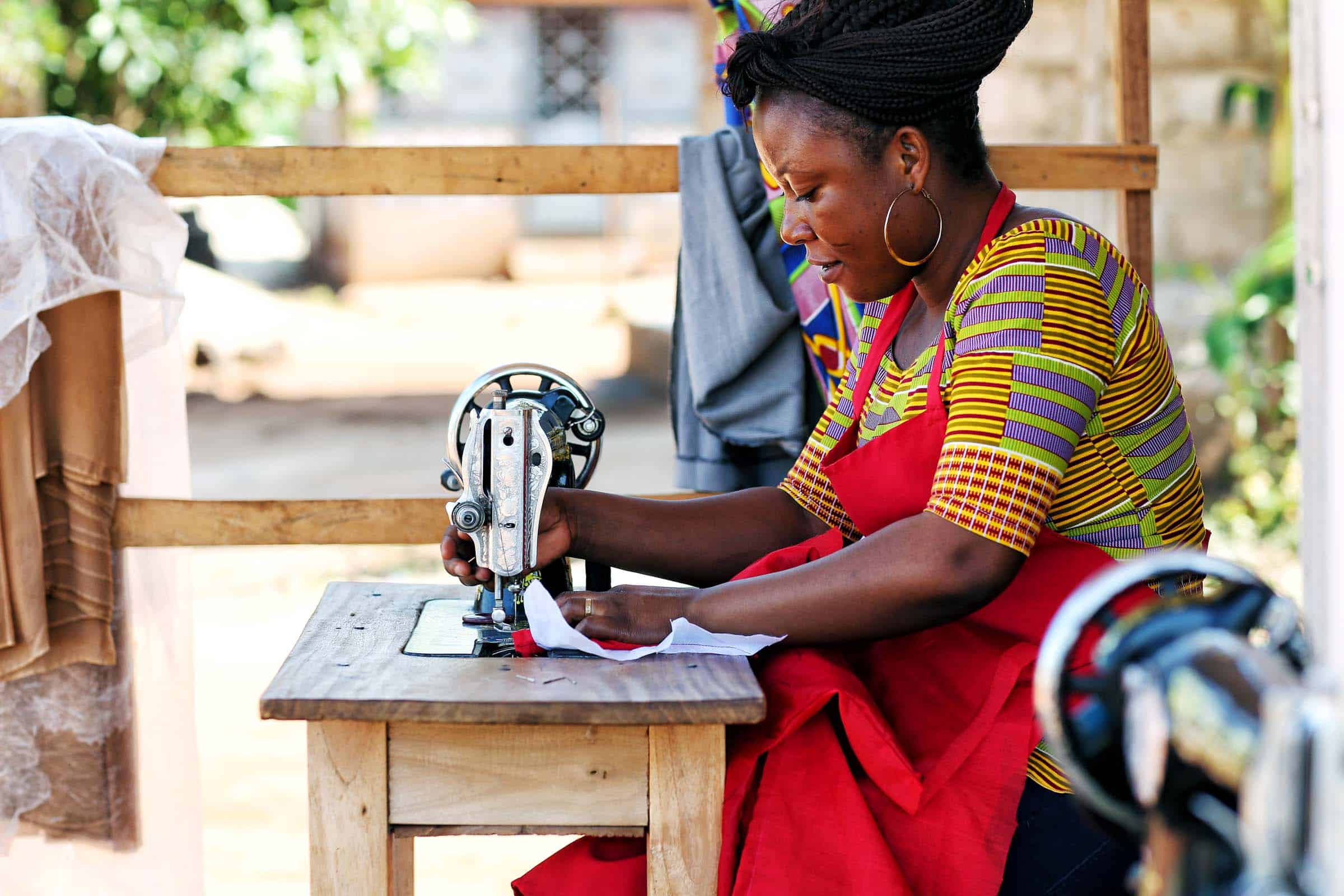 Bea works at her shop.  She owns a small seamstress shop in Techiman offering custom made clothing as well as alterations.